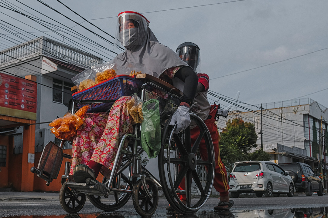 Seorang anak membantu mendorong kursi roda ibunya saat berjualan makanan keliling di ruas jalan durian,Kota Pekanbaru, Riau. Berjuang untuk ekonomi di tengah pandemi, mereka menggunakan pelindung wajah dan masker untuk melindungi diri dan pembeli dari penyebaran Covid-19.