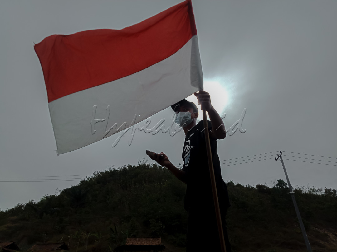 Foto ini diambil pada tanggal 15 agustus 2021<br />
<br />
terlihat seorang pemuda membawa bendera merah putih yang akan dikibarkan di atas gunung yg ada di belakang pemuda tersebut. 