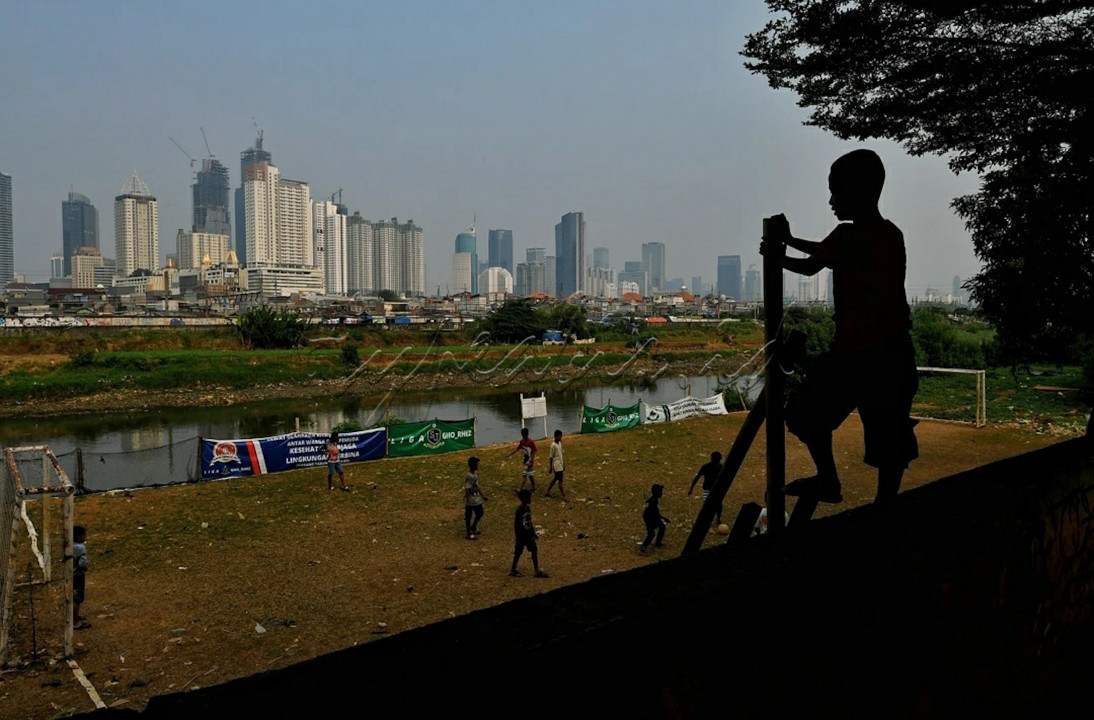 Anak-anak bermain sepakbola di bantaran kali Ciliwung, Jakarta, dengan latar belakang gedung bertingkat. 
