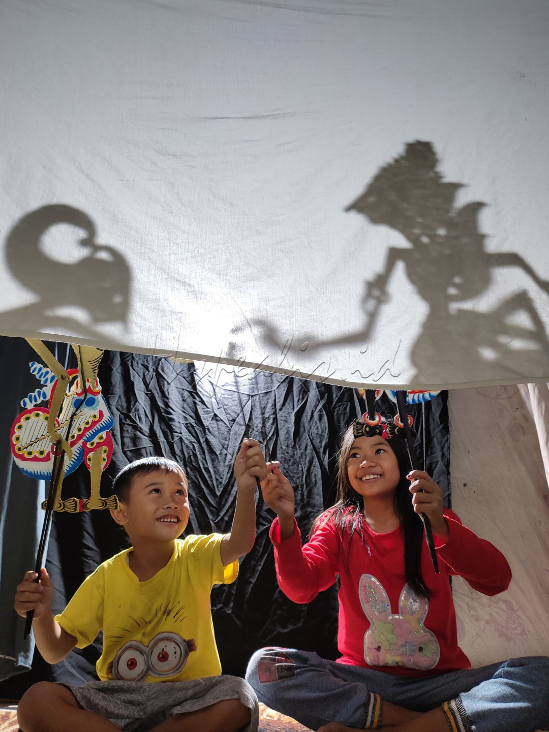 Dua anak sedang asyik memainkan wayang
