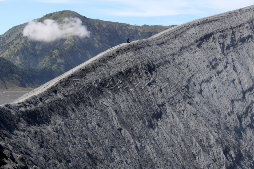 Turis Lokal melintasi bibir kaldera Gunung Bromo, Probolinggo, Jawa Timur. Bibir kawah yang terbentuk oleh gunung api ini memiliki bentuk yang cukup runcing karena tidak cukup waktu untuk mengalami proses pelapukan sehingga kontur menjadi landai. hal ini dipengaruhi pula oleh curah hujan yang cukup tinggi sehingga mampu mengikis tanah di punggungan bibir kawah dan merosot ke tempat yang lebih rendah
