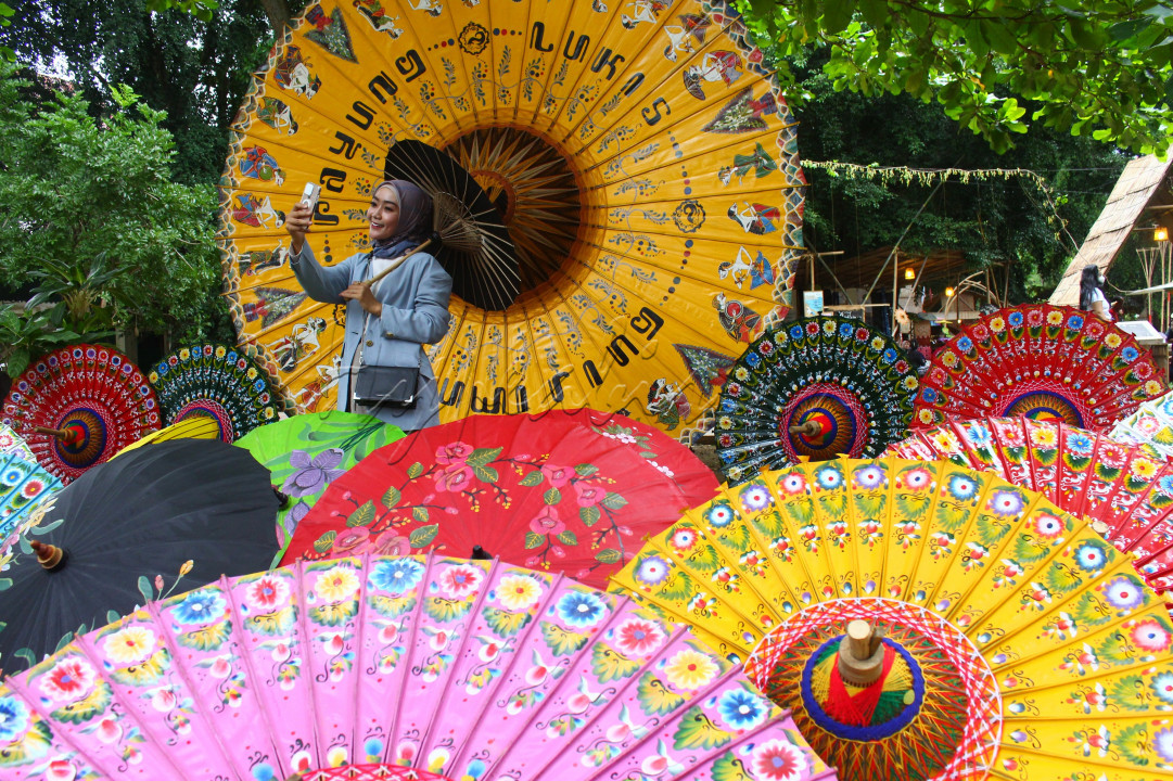 Seorang wisatawan sedang menikmati pesona payung lukis pada event Festival Payung Indonesia di Taman Balekambang Solo dengan berfoto selfie ceria, Pada event Festival Payung Indonesia ini memamerkan puluhan payung hasil produksi UMKM dari Jawa hingga papua. Produk-produk payung seantero Nusantara itu mewarnai salah satu taman bersejarah di Kota Solo. Festival yang menampilkan berbagai seni kreasi payung tersebut digelar untuk melestarikan kerajinan payung tradisional nusantara sekaligus upaya mempertemukan pelaku industri kreatif payung dan penggiat seni karnaval.<br />
