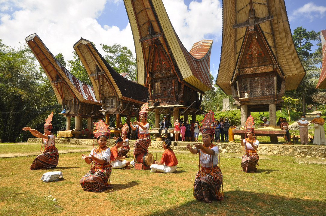 Remaja puteri memperagakan tarian adat Toraja dengan latar belakang rumah tradisional Tongkonan